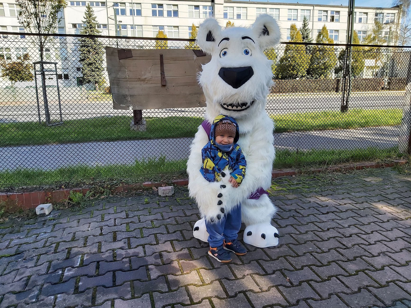 Na fotografii widnieje strój reklamowy w postaci białego misia pozujący do zdjęcia w siedzibie firmy Elabika